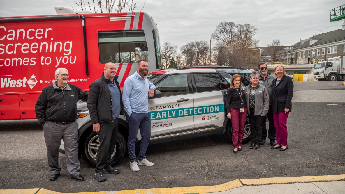 A group of seven people stand beside a Fox Chase Cancer Center–Temple Health vehicle and a large mobile cancer screening bus