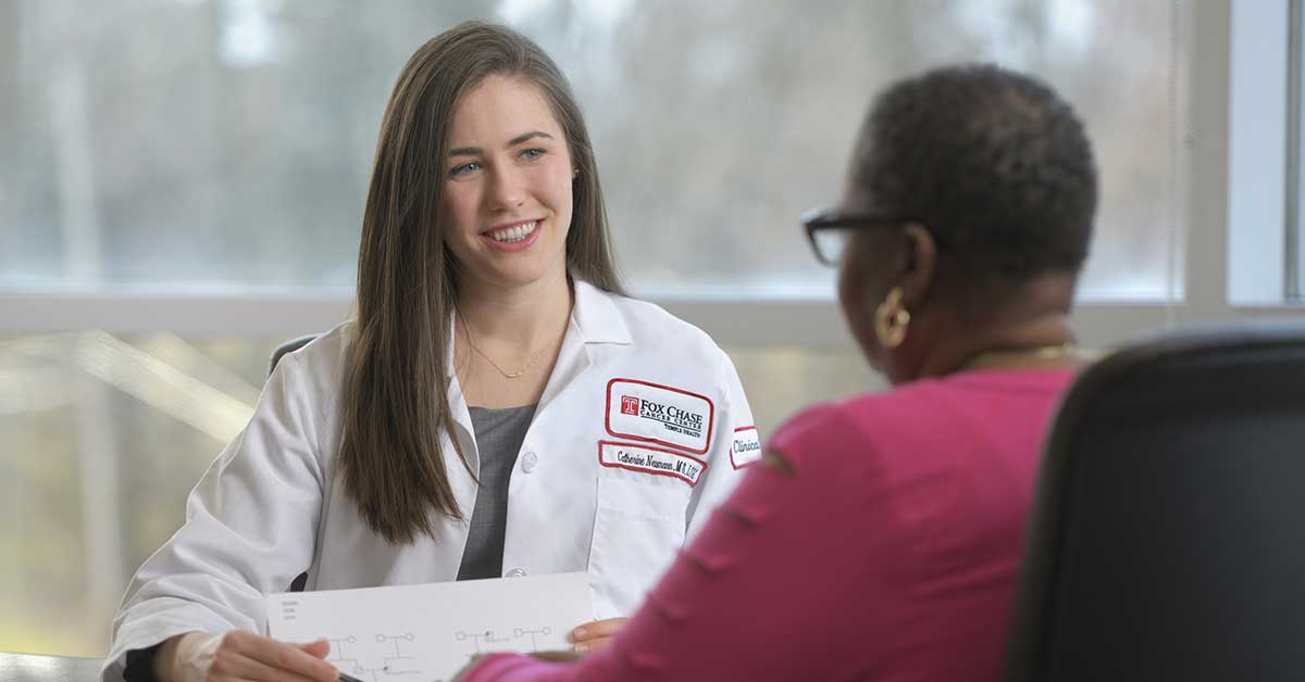 A Fox Chase doctor sits at a table across from a patient, holding a paper in their hands and smiling.