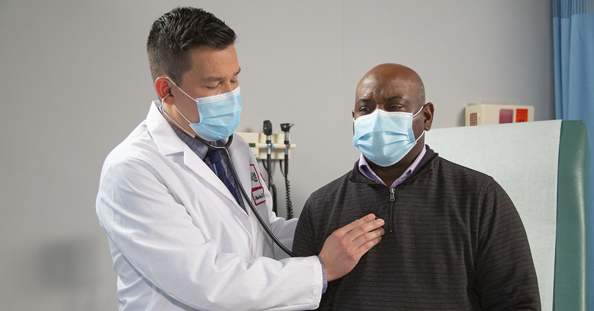 A Fox Chase doctor holds a stethoscope to a patient's chest inside of a medical room.