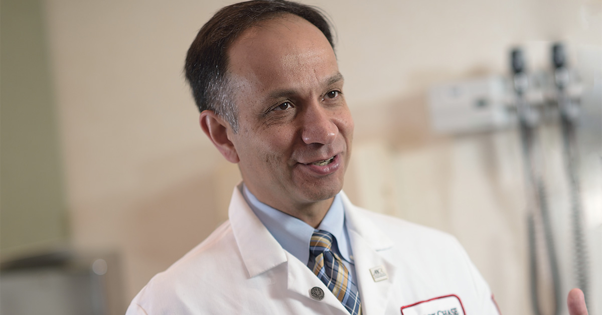 A closeup photo of a Fox Chase doctor speaking to someone off camera while in a medical room, smiling.