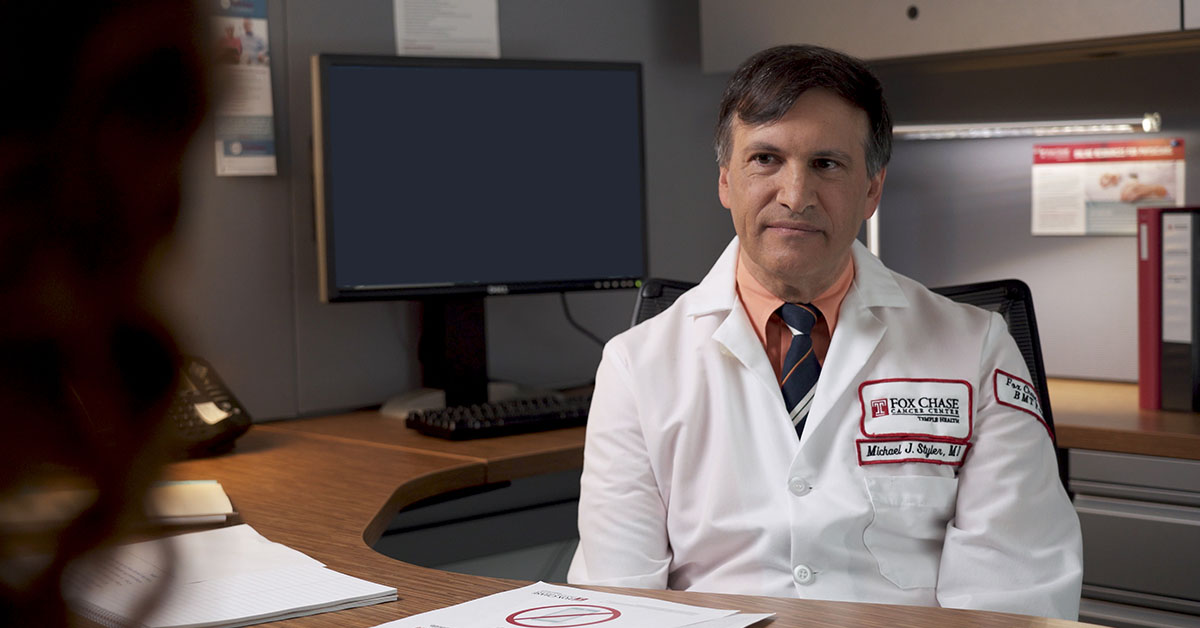 A photograph of a Fox Chase doctor sitting behind a desk, speaking with someone on the other side of it.