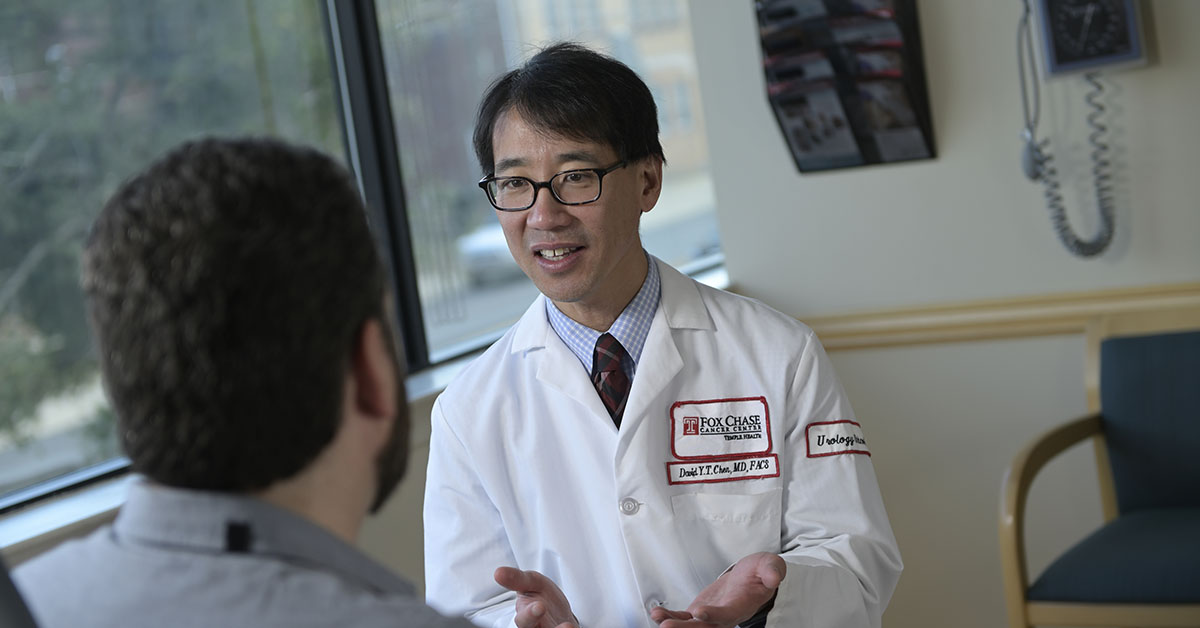 A Fox Chase doctor smiles as they speak with a patient, sitting across from each other in front of a window.