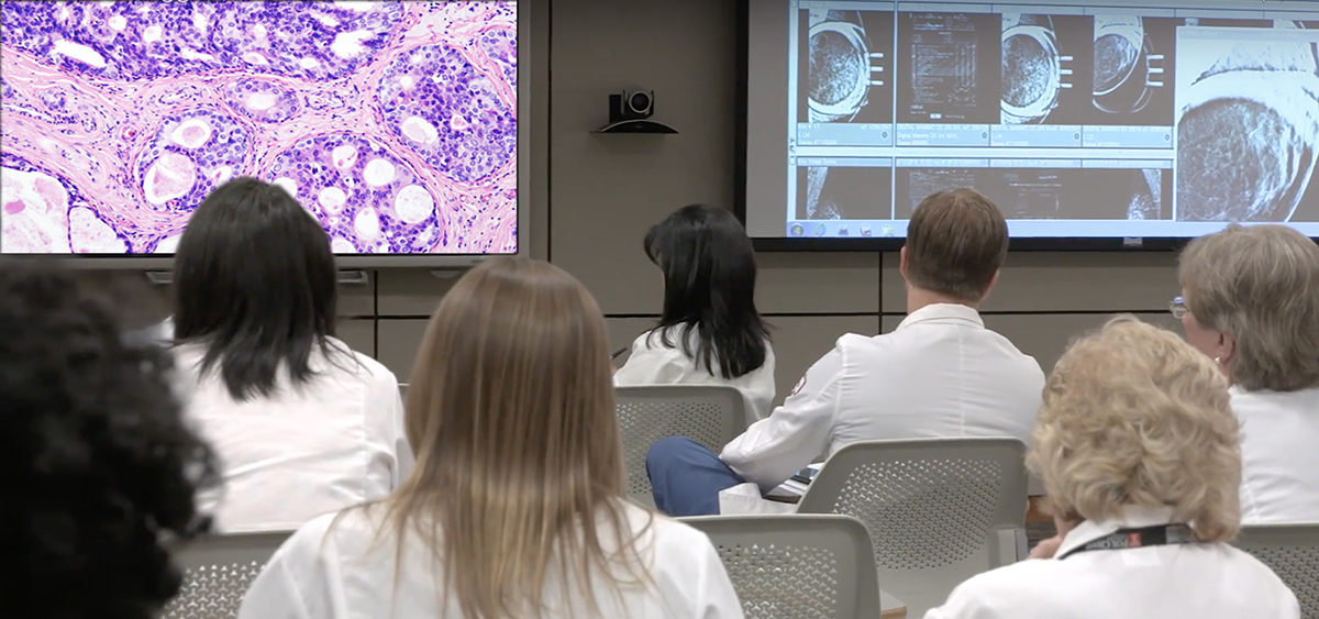 A photo from the back of a classroom showing several medical professionals in chairs all looking at a board at the front.