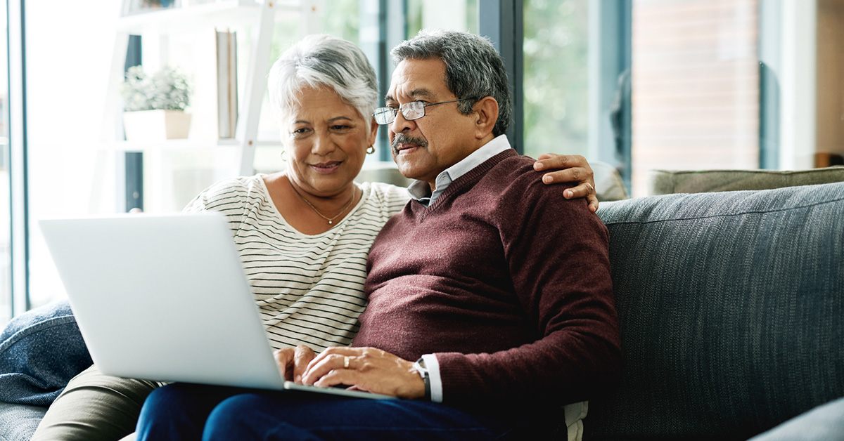 Two people huddle closely together on the couch, using a laptop.