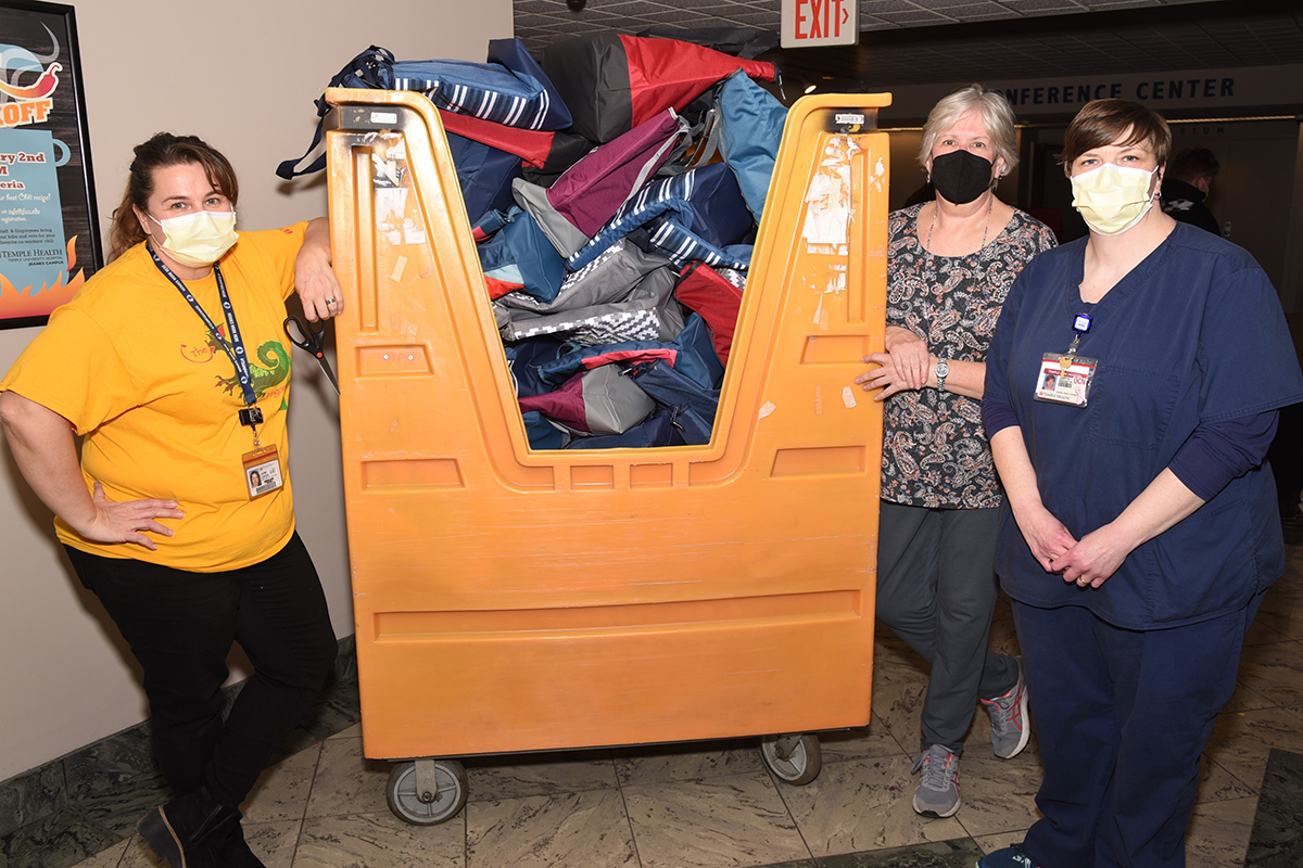 3 women standing in front of a large yellow cart filled with bags