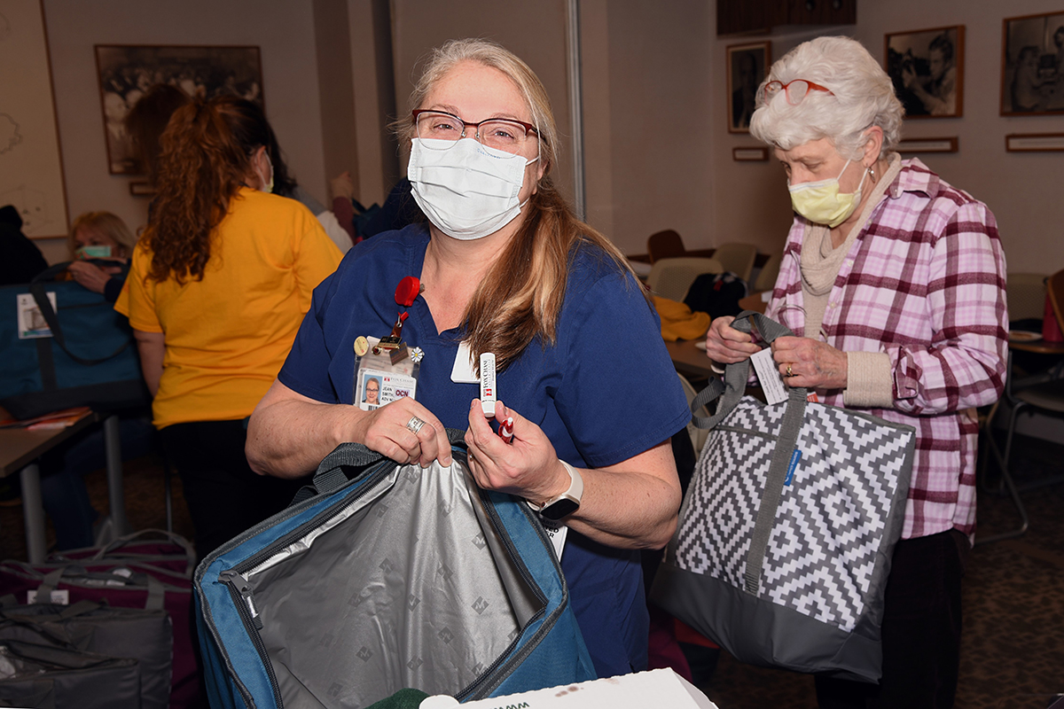 A woman holding a bag and a pen in front of other women working on staffing bags