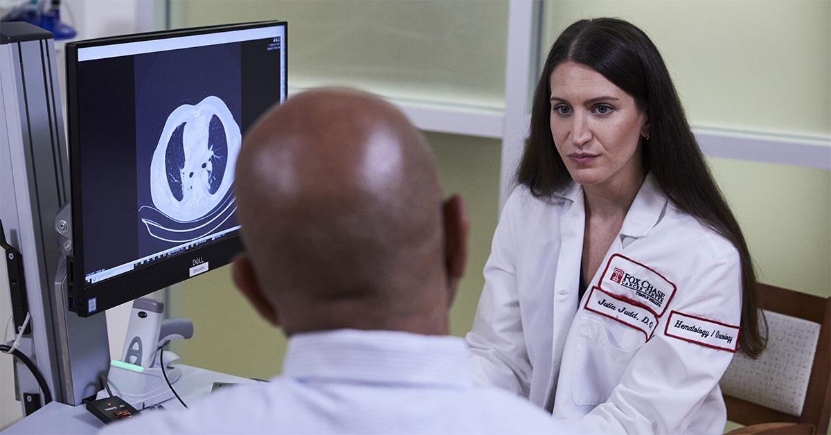 A Fox Chase doctor converses with another person in front of a screen with results from a medical imaging test on it.