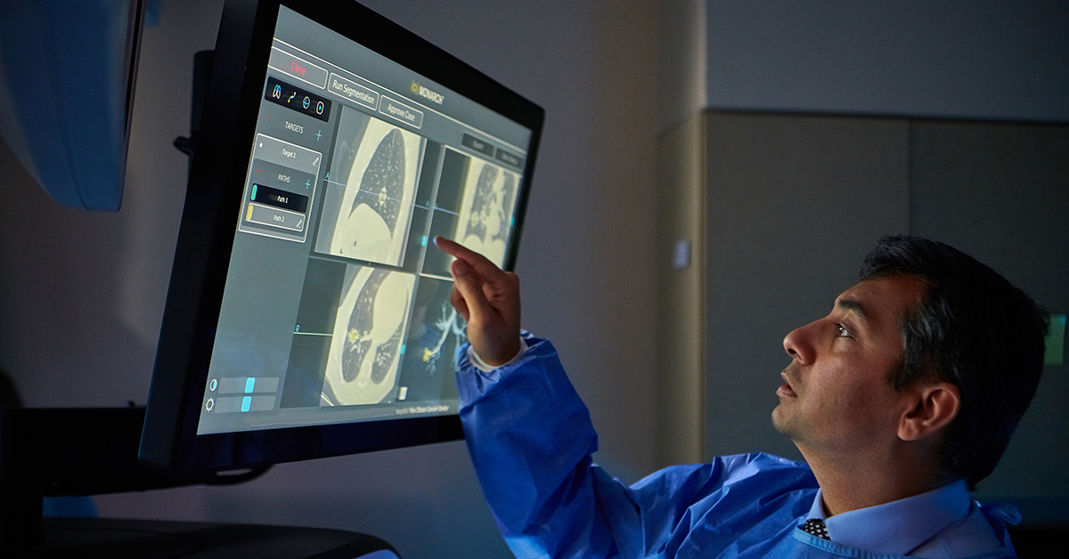 A Fox Chase doctor stands in a dark room, interacting with a screen displaying medical imaging results.