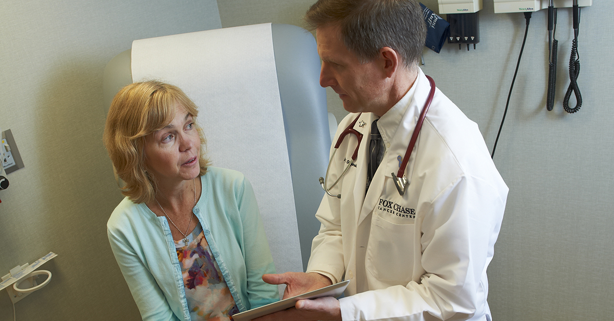 A Fox Chase doctor speaks closely with a patient, gesturing to a clipboard in his hands.