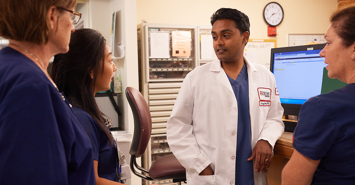 A photograph of Dr. Reddy speaking with three other Fox Chase medical professionals in a medical room, with a computer screen behind him.