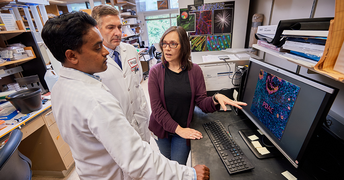 A photo of three Fox Chase doctors talking in a lab, with a computer screen in front of them.