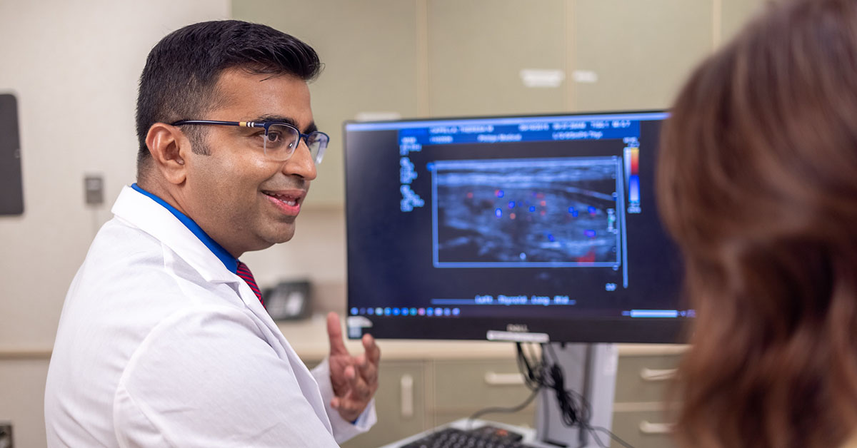 A Fox Chase doctor converses with another person in front of a screen with results from a medical imaging test on it.