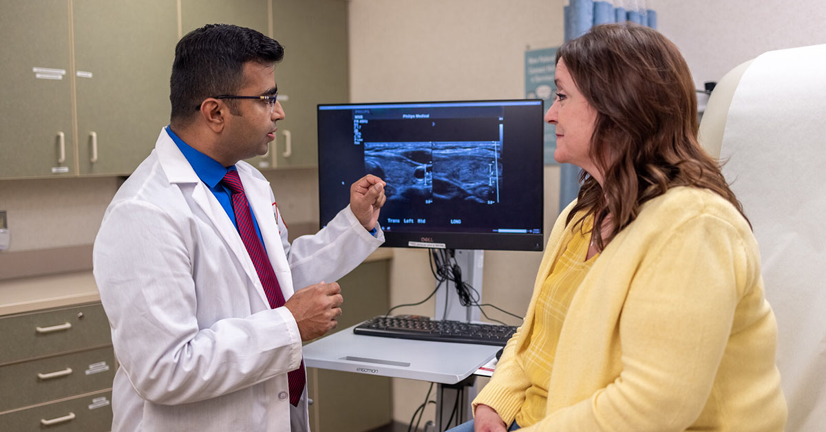 A Fox Chase doctor converses with a patient in a medical room with results from an imaging test on a screen between them.