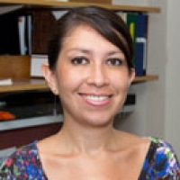 A portrait shot of Daniela Ariaza-Olivera smiling at the camera, with various books and files in the background.