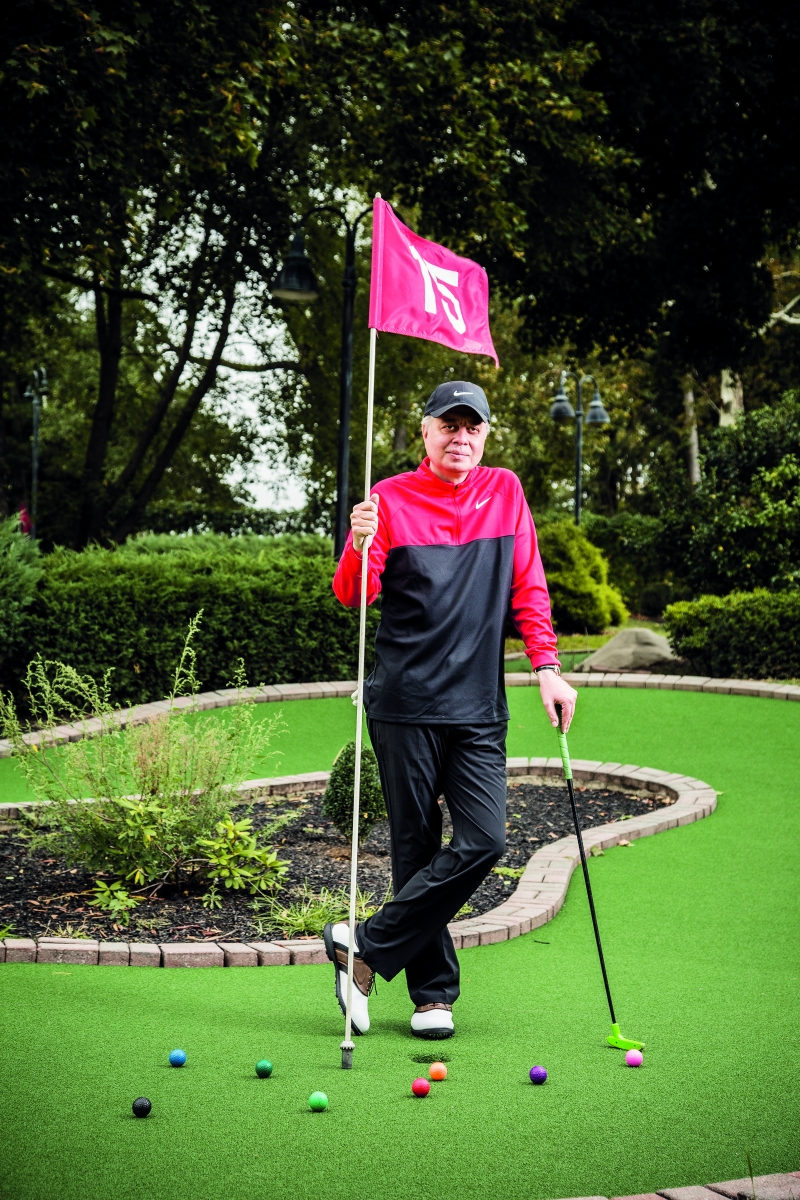 Mahmood Saeed, posing by a hole at a golf course and holding a pink flag in one hand.