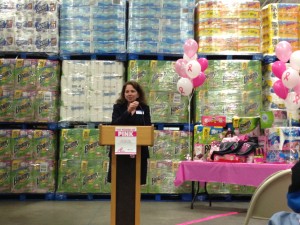 A photo of a medical professional at a podium next to the table with pink balloons, speaking to the audience.