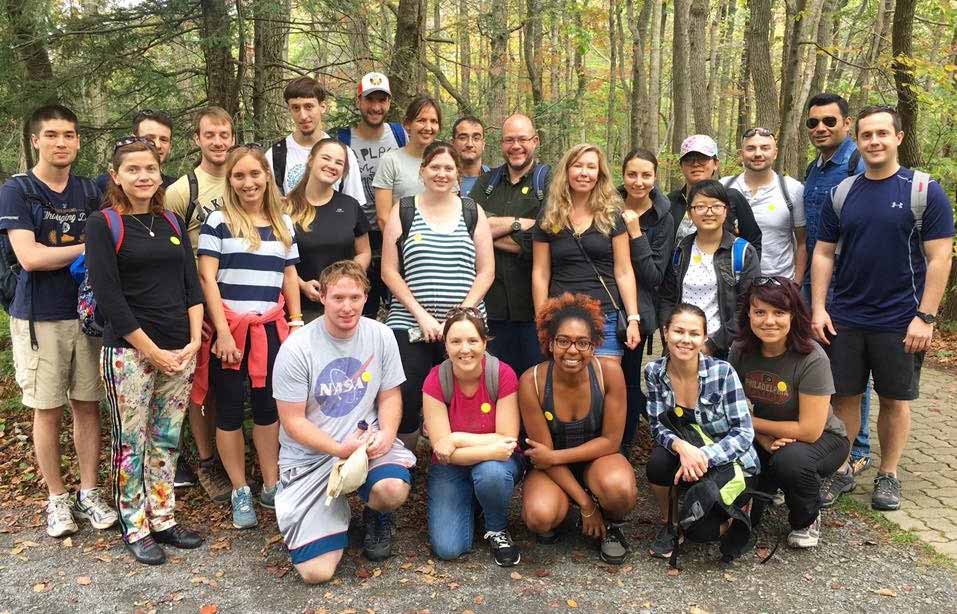 A photograph of a group of people in a woody area, smiling at the camera.