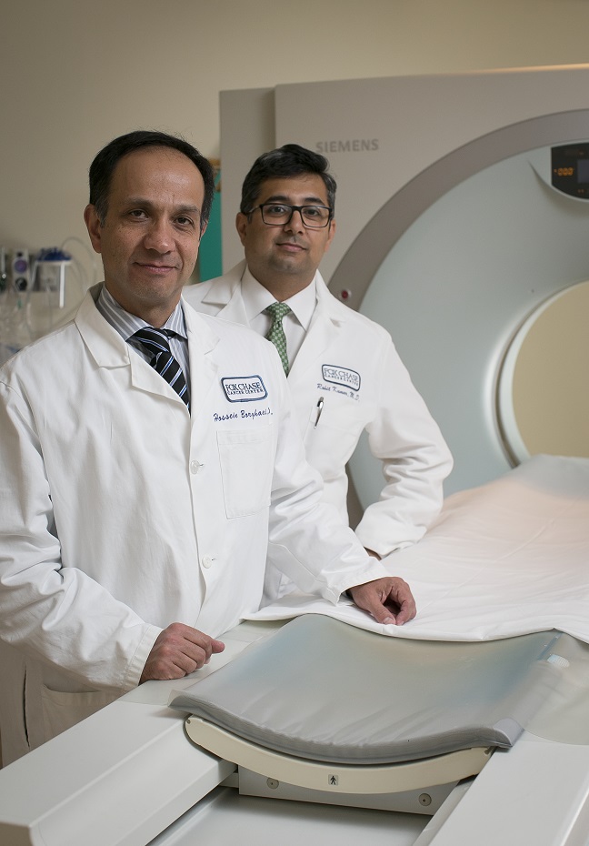 Two Fox Chase doctors standing in front of a medical imaging device smile at the camera.