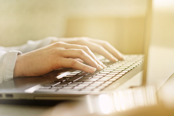 Photograph of a woman typing on a laptop