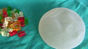 A photograph of a pile of gummy bears next to a gel breast implant.