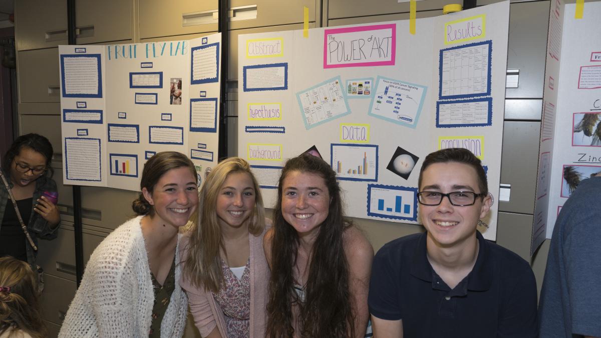 A photograph of four students, smiling as they pose in front of their posters.