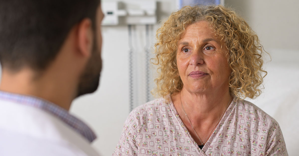 A photograph of a doctor and patient facing each other in a medical room.