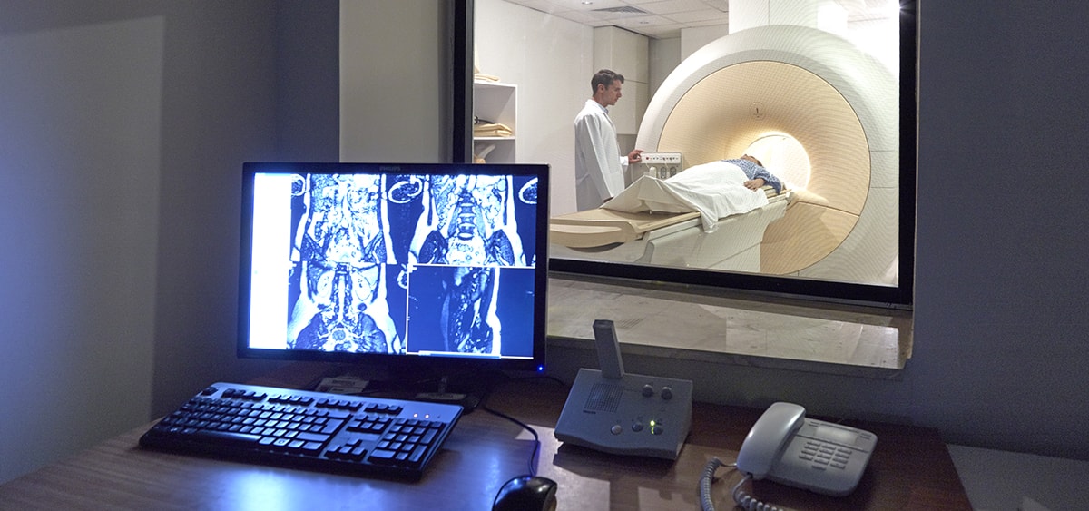 A photograph of a medical professional standing next to a patient inside of a large medical imaging machine.