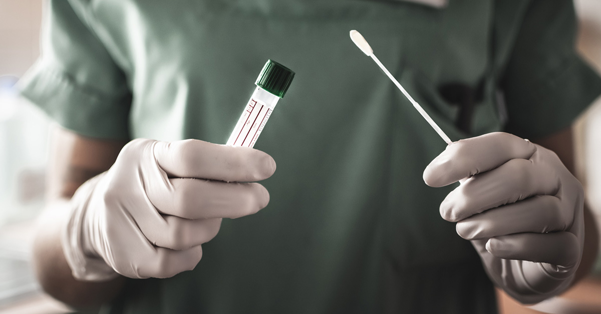 A close up photograph of medical professional's upper body, an empty collection vial and a long cotton swab in their hands.