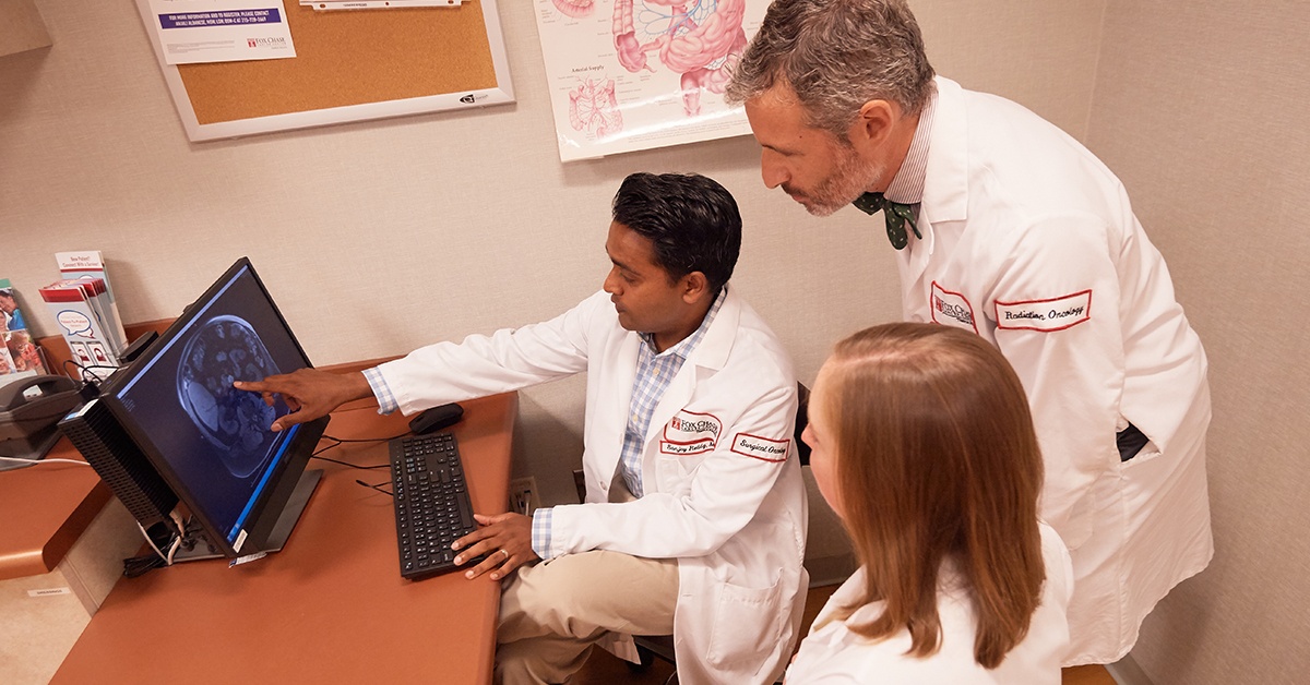 A photograph of three doctors around a computer discussing the displayed medical imaging results.