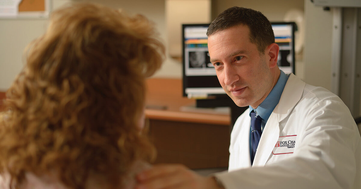 A closeup photo of a Fox Chase doctor gently putting his hand on a patient's shoulder.