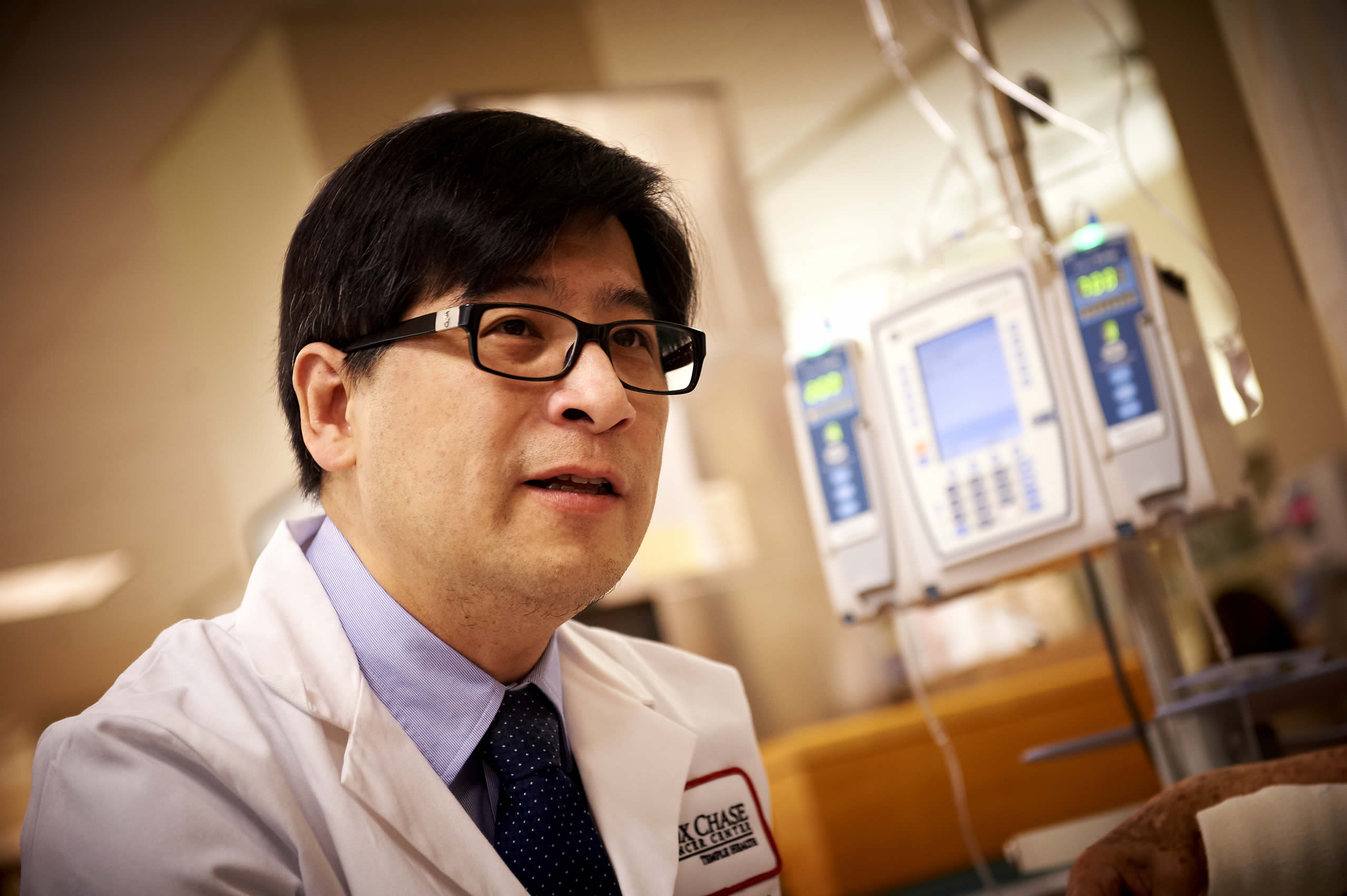 A closeup photo of a Fox Chase doctor's face speaking to someone off camera, in a medical room with a blurred background.