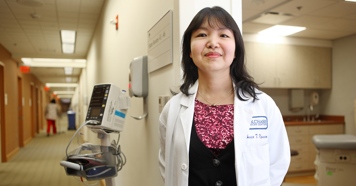 A photo of Dr. Minhhuyen T. Nguyen standing in a doorframe of a hospital hallway, smiling at the camera.