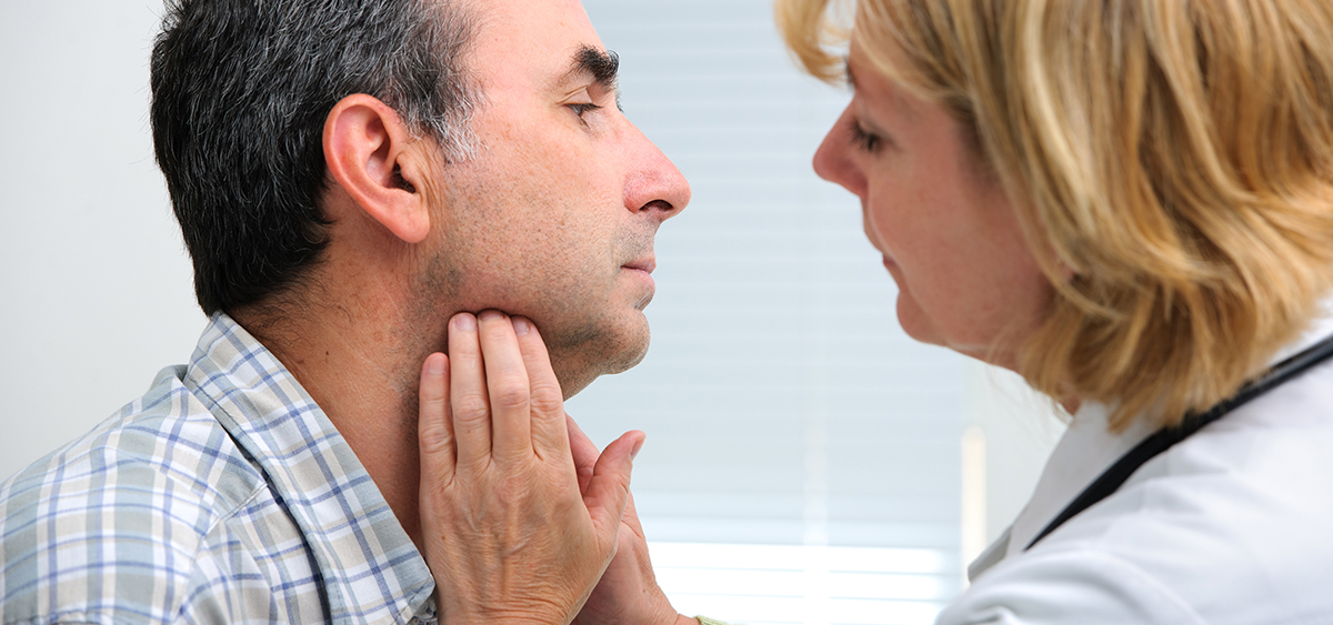 A photograph of a medical professional using her hands to feel the underside of a patient's chin.