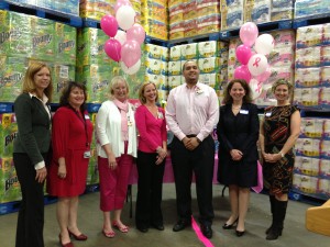 A photograph of seven people standing together in front of a table with pink balloons inside of a store, smiling at the camera.