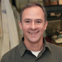 A portrait shot of a person in a brown polo smiling at the camera.