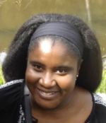 A close up photograph of Sajitha Anthony's face, smiling at the camera as they stand outside.