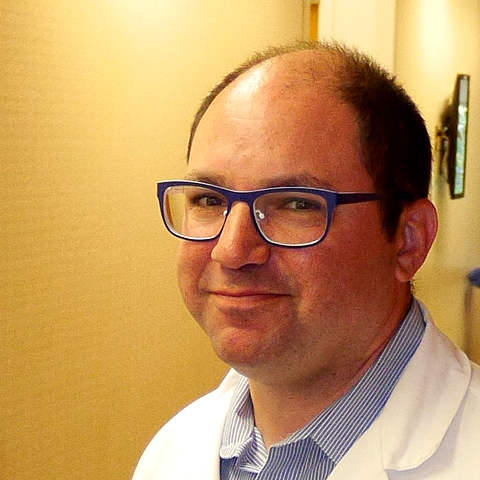 A closeup photo of Dr. Jeffrey M. Farma, MD, FACS, standing by a wall and smiling at the camera.