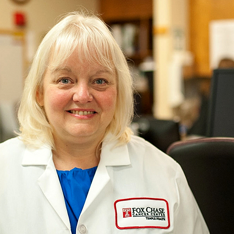A portrait shot of a medical professional wearing a white Fox Chase Cancer Center jacket, smiling at the camera.