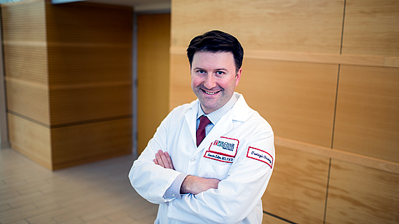 A Fox Chase doctor stands in front of a wooden wall, smiling at the camera.