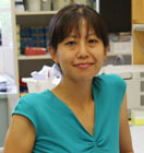 A portrait shot of Shoko Nogusa in a laboratory, smiling at the camera.
