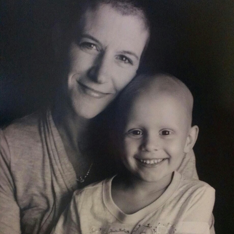 A sepia photograph of Sheila Koreck sitting with her four year old daughter in her lap, both smiling at the camera. 