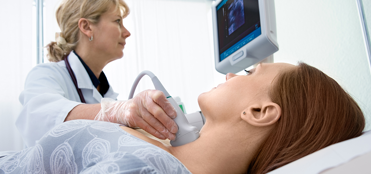 A photograph of a medical professional looking at a screen while giving a patient an ultrasound of their neck.