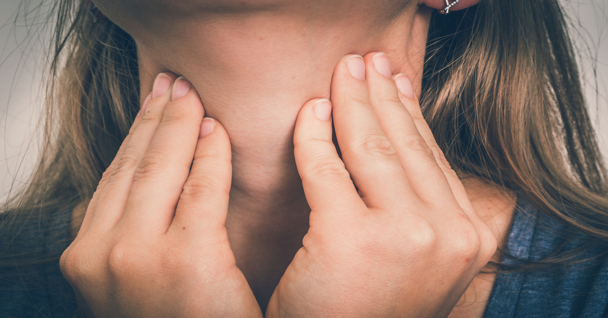 A closeup photo of a person pressing on either side of their neck with their fingertips.