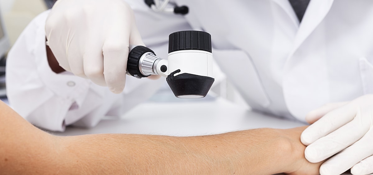 A closeup photo of a medical professional holding a handheld tool up to a patient's arm to help them examine it.