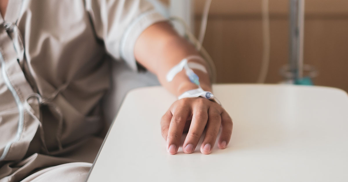 A closeup photo of a patient's arm as they sit in a chair and receive an IV through their wrist.
