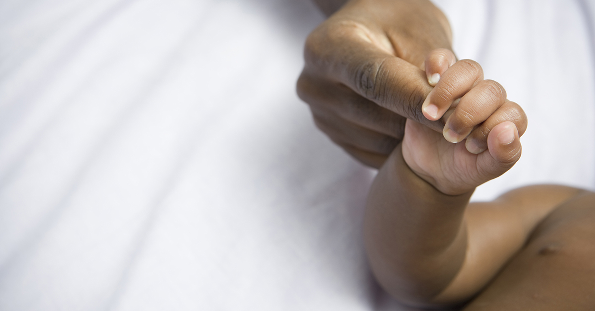 A closeup photo focused on the hand of a baby clutching a person's finger tightly.