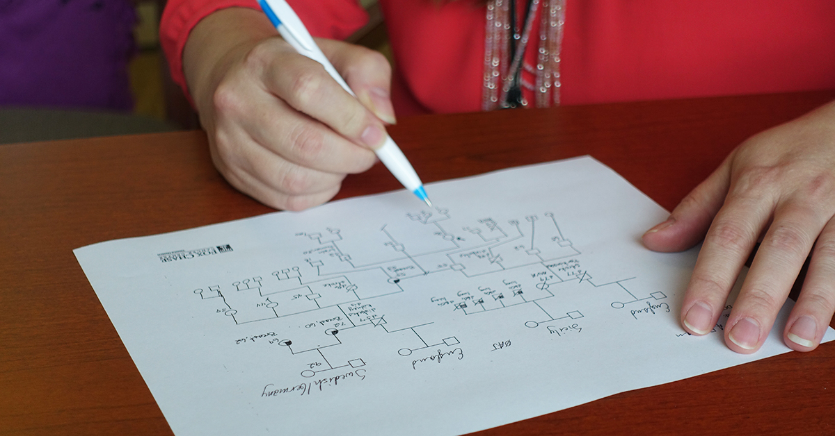 A person holds a pen to a piece of paper as they map various hereditary genes on it.