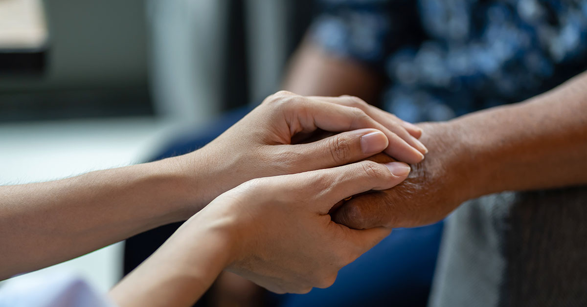 A closeup photo of a person using both of their hands to gently clasp around another person's hand.
