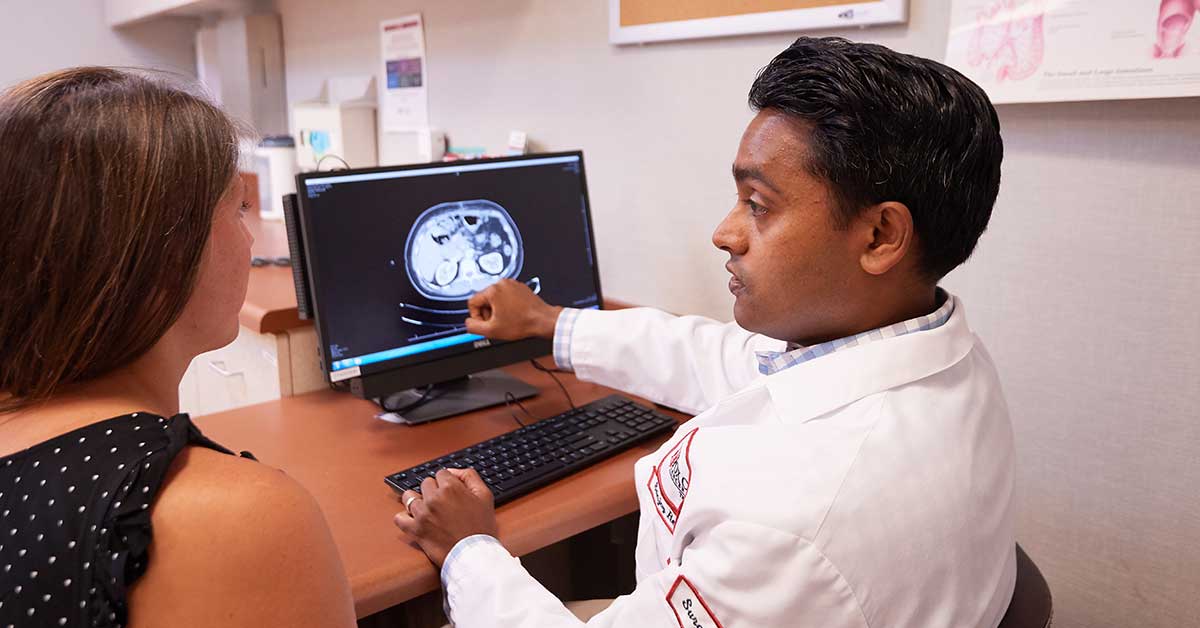 A photo of a Fox Chase doctor and a patient sitting at a desk, while the doctor gestures at the screen.