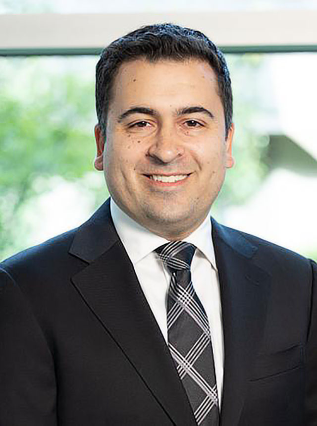 A close-up of Justin I. Friedlander, a male urologist, wearing a black suit with a white shirt, smiling. 